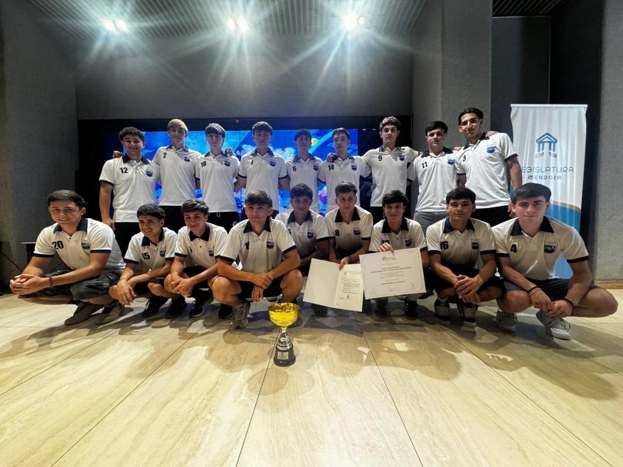 El plantel fue reconocido por su desempeño en el Torneo Argentino de hockey sobre césped, un logro que refleja años de trabajo, resiliencia y el aporte clave de las familias y los clubes de Mendoza. En la planta baja del edificio Margarita Malharro de Torres de la Legislatura de Mendoza se realizó un emotivo acto para distinguir al equipo Campeón Argentino Sub 19 de Hockey sobre Césped masculino, perteneciente a la Asociación Mendocina de Hockey, por el desempeño alcanzado en el Torneo Argentino organizado por la Confederación Argentina de Hockey sobre Césped. La propuesta, impulsada por la senadora Fernanda Sabadin, puso en valor el trabajo de la delegación que obtuvo el título nacional en octubre de este año, en el certamen disputado en Mendoza. Para la autora de la iniciativa, este logro representa la culminación de un proceso sostenido de formación, disciplina y compromiso, fruto de años de entrenamiento y dedicación. El conjunto mendocino logró victorias claras ante Chubut, Salta y Entre Ríos, superó a Buenos Aires en semifinales y se coronó campeón frente a Litoral en el partido decisivo. Ese recorrido reafirmó no solo su calidad técnica, sino también la fortaleza mental que caracteriza a este plantel, capaz de sostener objetivos y sobreponerse a cada desafío. El crecimiento de esta disciplina en la provincia, sumado al desempeño del hockey masculino, constituye un aporte al deporte local y nacional por el prestigio que proyecta. Durante el acto, la senadora Sabadin destacó la dimensión formativa del deporte y el rol de los clubes mendocinos en la construcción de valores. Señaló que detrás de cada logro hay esfuerzo, constancia y resiliencia, y subrayó el acompañamiento de las familias como parte fundamental de este proceso. Valoró además la identidad que Mendoza ha forjado en la disciplina y el modo en que los grupos se transforman en verdaderas comunidades que sostienen a los jugadores dentro y fuera de la cancha. El capitán del equipo, Juan Francisco Lorenzo, agradeció la distinción y recordó los años de entrenamiento que demandó alcanzar este objetivo, mencionando el trabajo colectivo y el apoyo permanente de las familias. También habló Valentino Moretti, quien resaltó la importancia de visibilizar el esfuerzo que hay detrás de la obtención del título y sostuvo que este logro es un impulso para las próximas generaciones que representarán a Mendoza. Del acto participaron los jugadores del plantel campeón, el cuerpo técnico integrado por Facundo Paredes, Gilberto Guerci, Marcos González, Marcos Sánchez y Rolando Rivero, además de familiares, dirigentes y allegados. La actividad concluyó con la entrega formal de la distinción por parte de las autoridades legislativas, que declararon de interés al equipo mendocino por el desempeño alcanzado en el Torneo Argentino. El reconocimiento cerró una jornada cargada de emoción, en la que se remarcó que las puertas de la Legislatura permanecen abiertas para estas y futuras celebraciones deportivas.